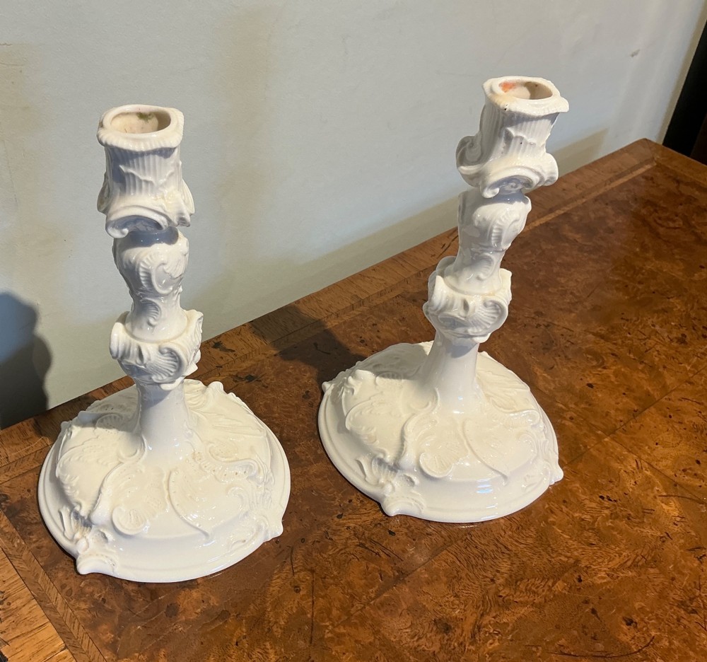 A pair of white glazed porcelain candlesticks featuring ornate Rococo relief moulding and scrollwork bases. View III