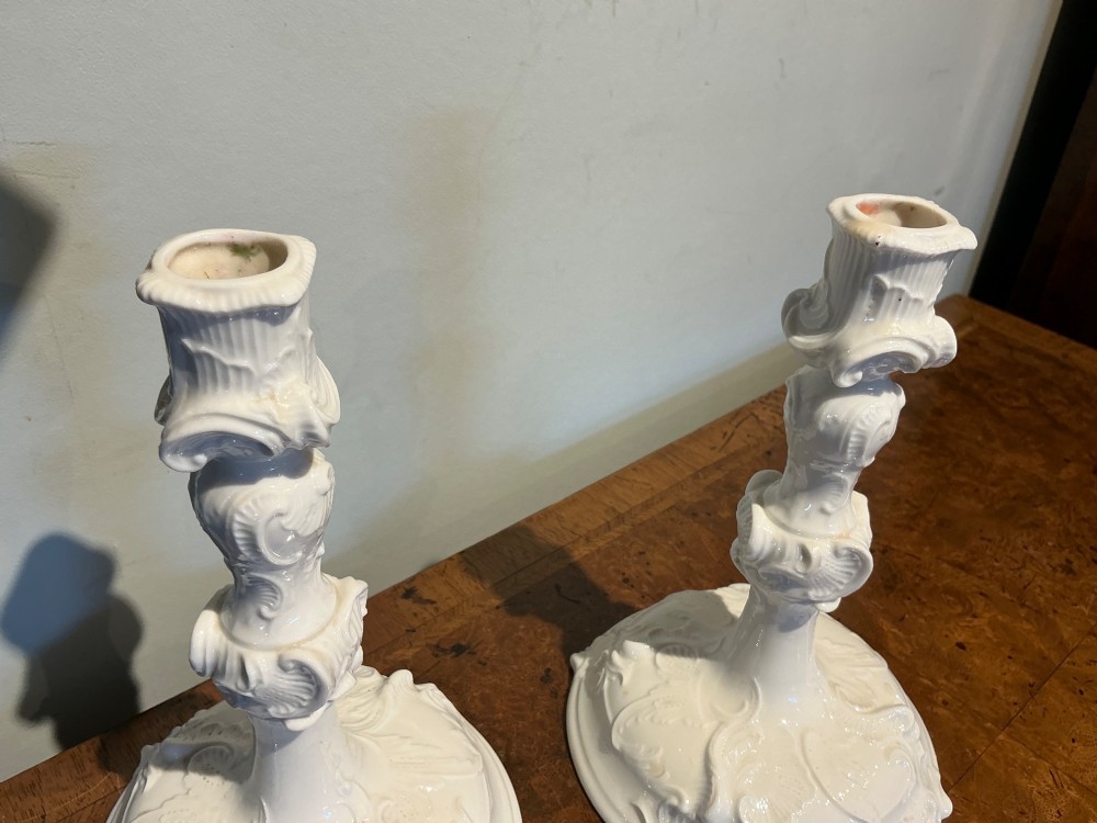 A pair of white glazed porcelain candlesticks featuring ornate Rococo relief moulding and scrollwork bases. View IV
