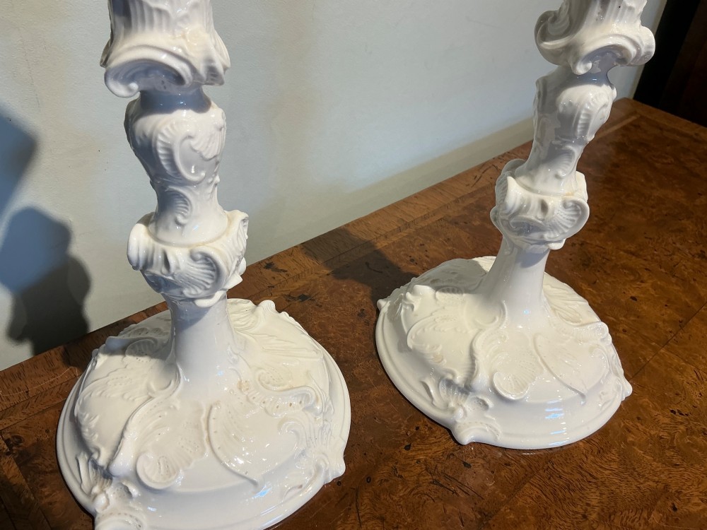 A pair of white glazed porcelain candlesticks featuring ornate Rococo relief moulding and scrollwork bases. View V