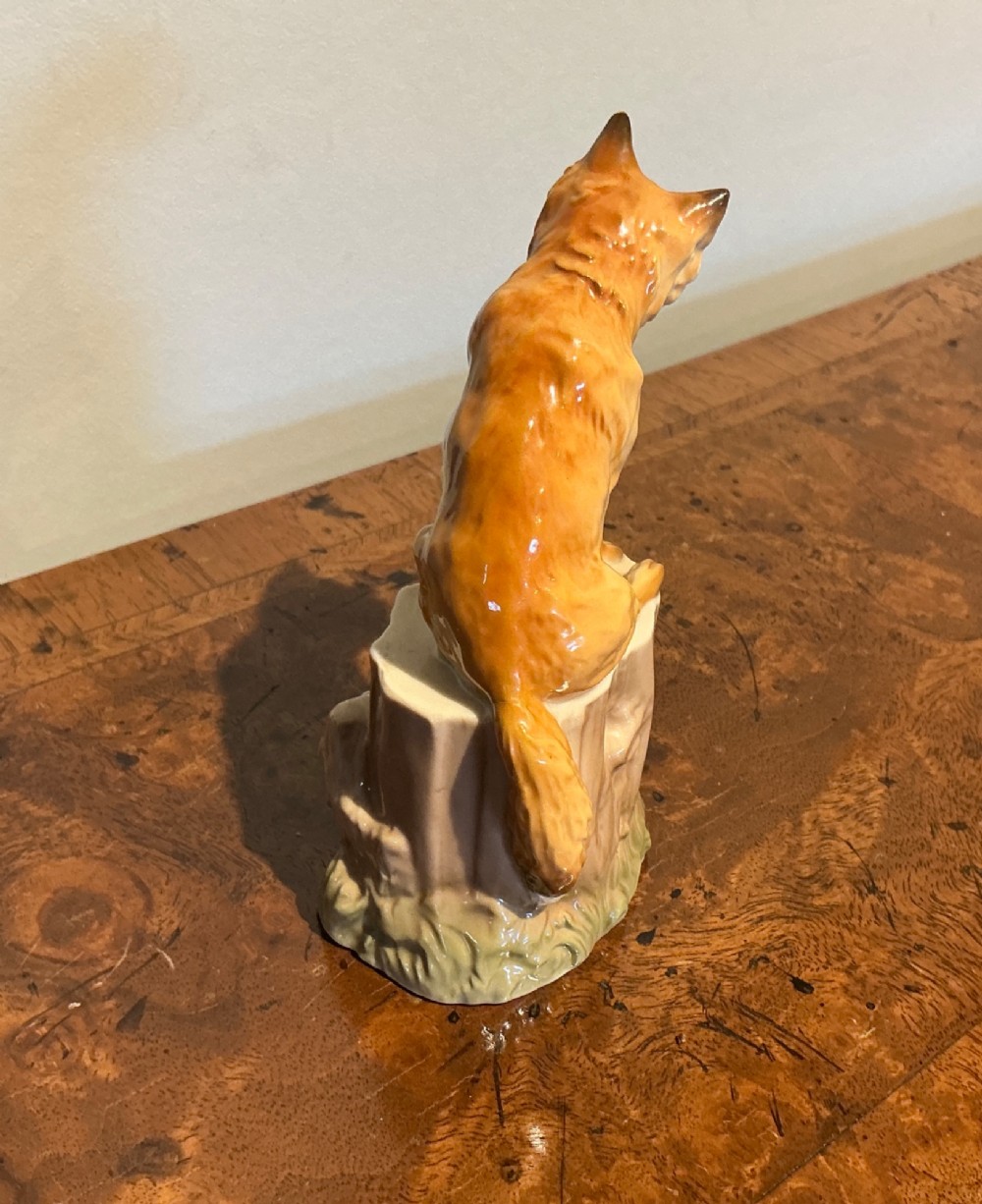 A glazed porcelain figurine depicting a rust-orange fox seated atop a moulded tree stump base with hand-painted details. View III