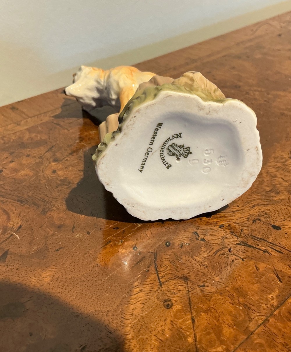 A glazed porcelain figurine depicting a rust-orange fox seated atop a moulded tree stump base with hand-painted details. View V