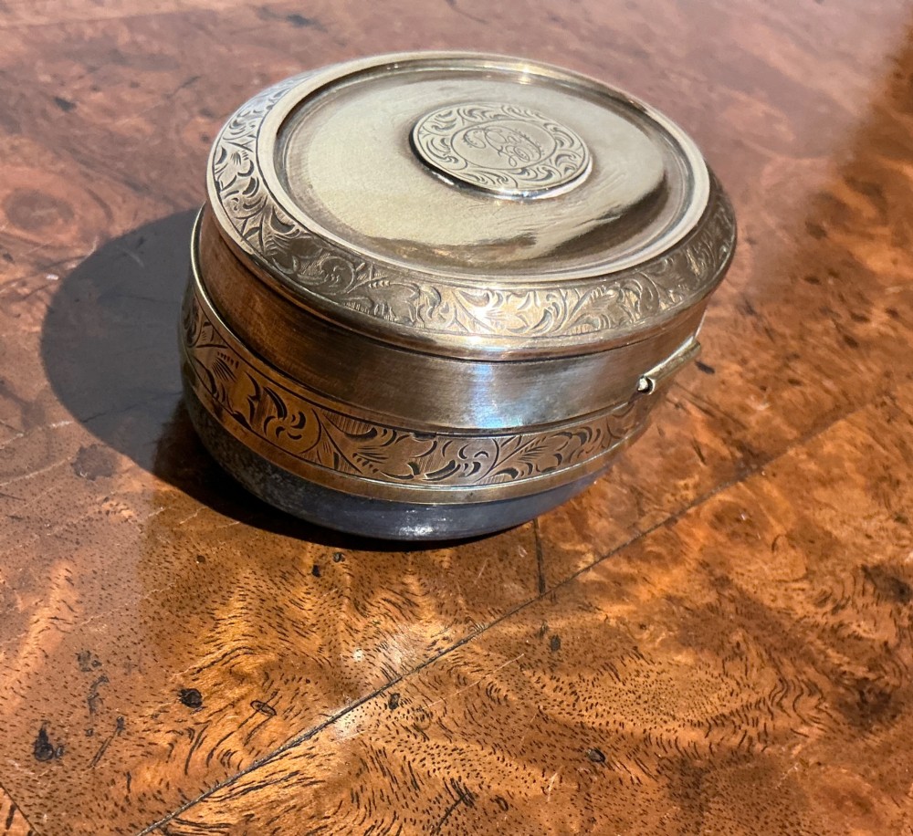 An oval Victorian brass travelling inkwell with detailed foliate engraving around the rim and a central monogram medallion. View IV