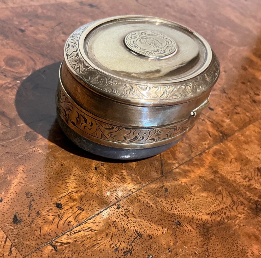 An oval Victorian brass travelling inkwell with detailed foliate engraving around the rim and a central monogram medallion. View V