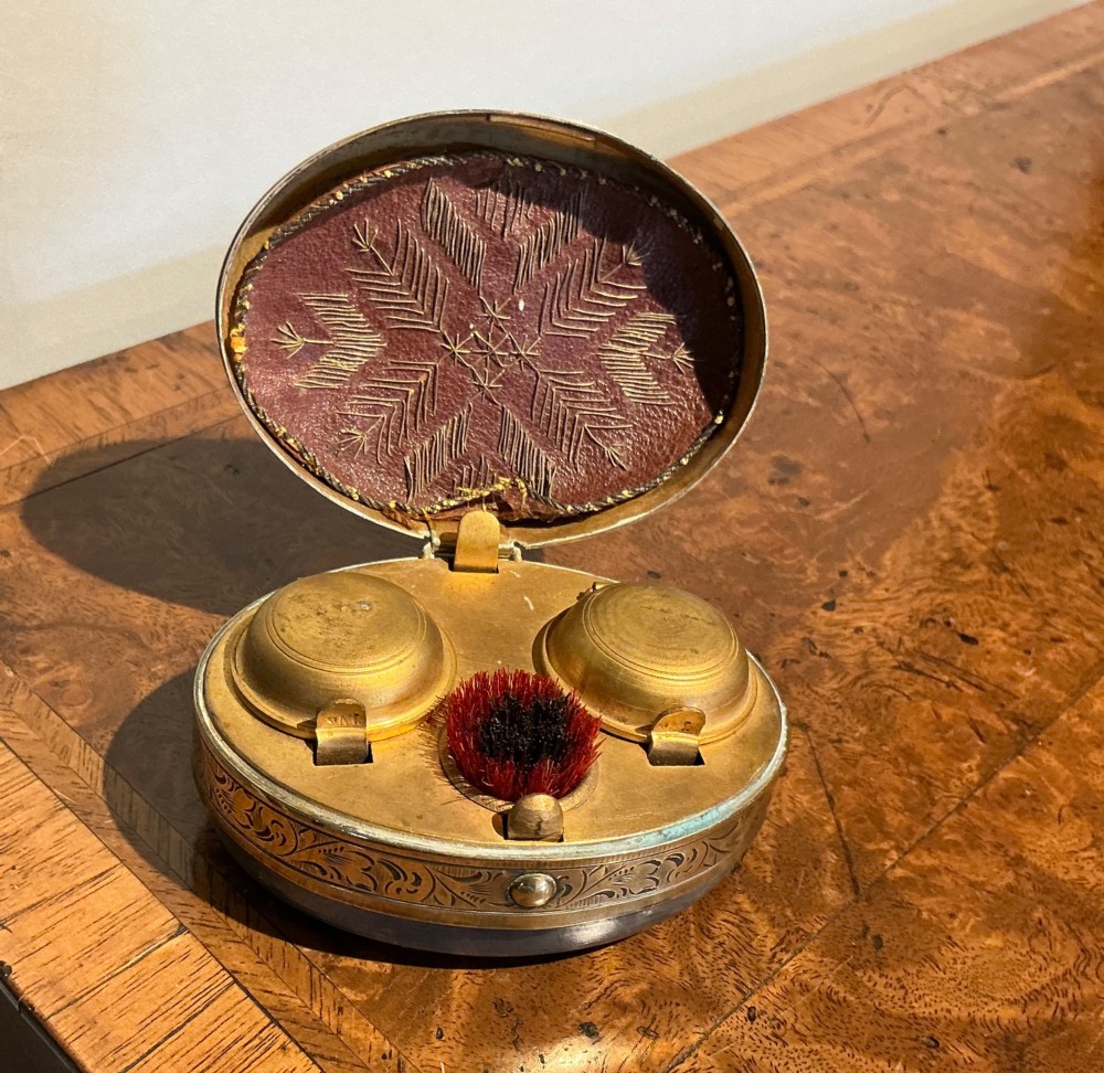 An oval Victorian brass travelling inkwell with detailed foliate engraving around the rim and a central monogram medallion. View VI