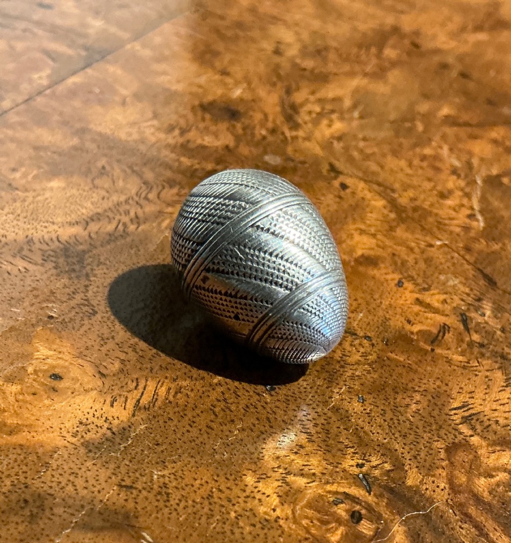 An egg-shaped sterling silver vinaigrette featuring intricate engine-turned geometric engraving and a central opening seam.