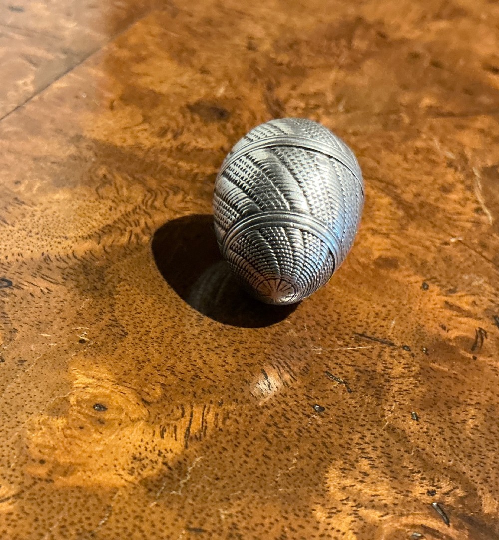 An egg-shaped sterling silver vinaigrette featuring intricate engine-turned geometric engraving and a central opening seam. View III