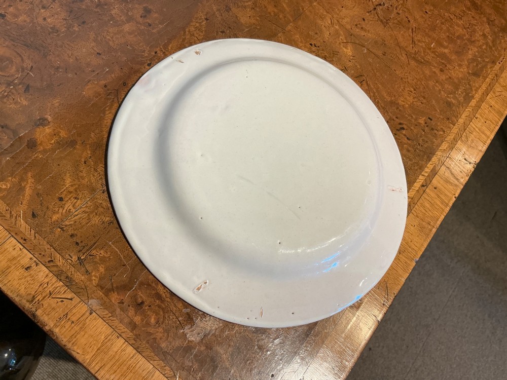 A circular off-white French faience plate decorated with a hand-painted crown, red fleur-de-lis emblems, a green laurel wreath, and a pink patterned rim. View IV