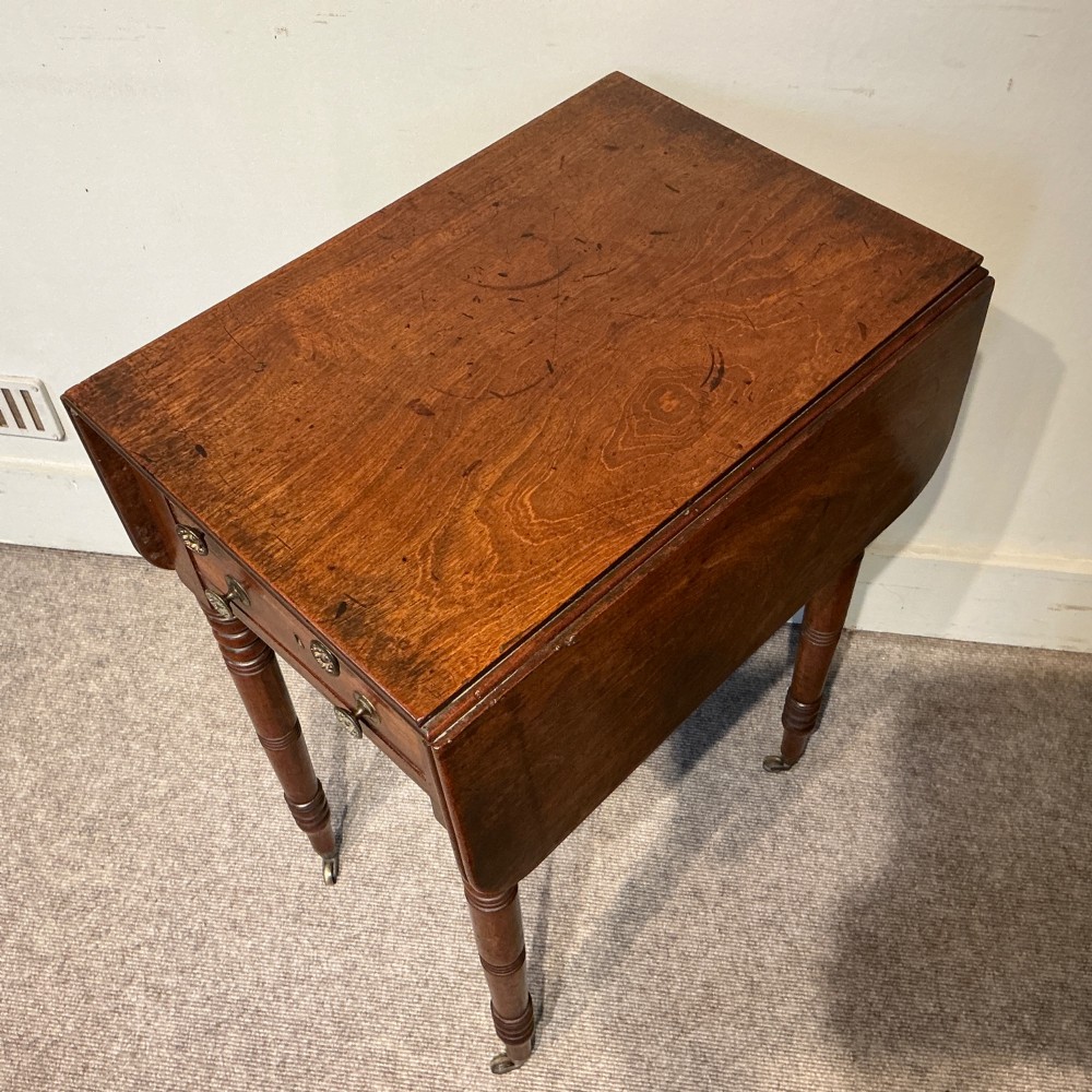 A dark mahogany Georgian Pembroke table featuring two drop leaves, twin drawers with brass knobs, turned legs, and brass castors. View III