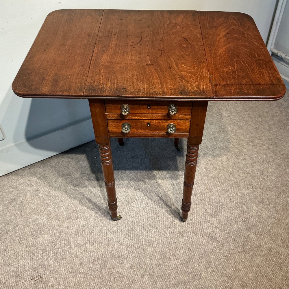 A dark mahogany Georgian Pembroke table featuring two drop leaves, twin drawers with brass knobs, turned legs, and brass castors. View IV