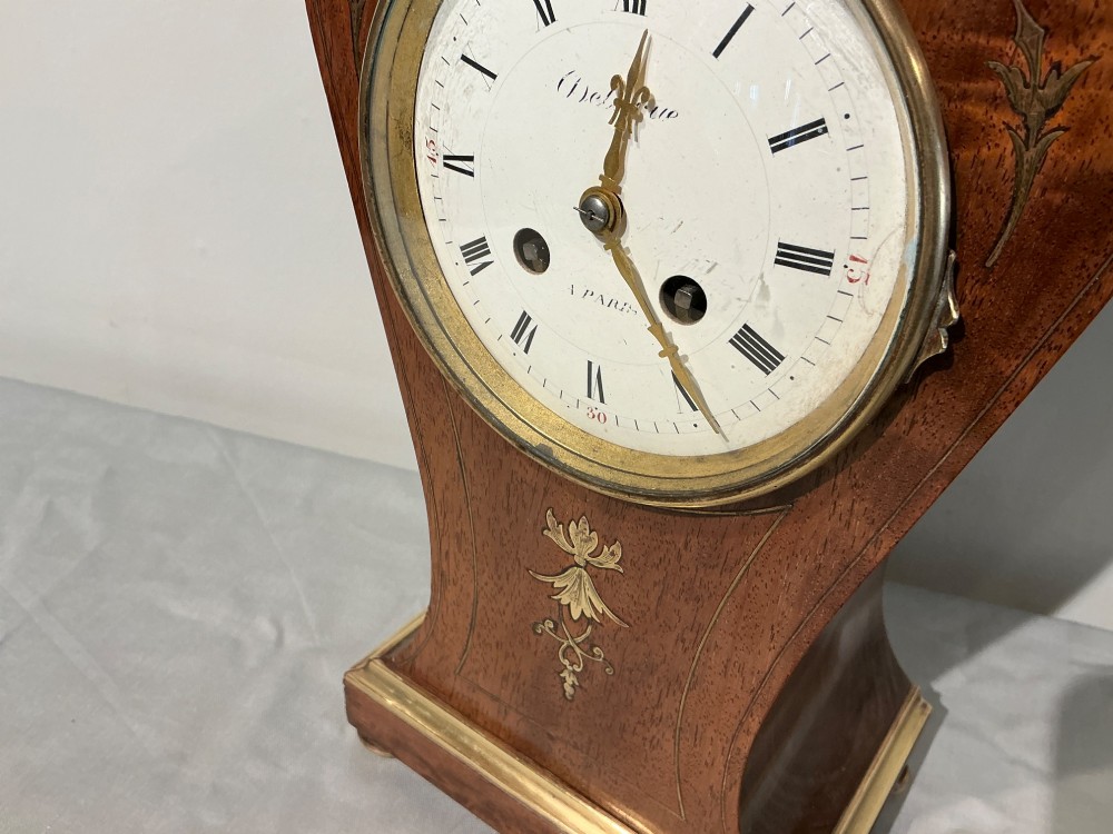An antique balloon-shaped mahogany mantel clock featuring inlaid brass floral details, a white enamel dial with Roman numerals, and a brass-trimmed plinth base. View II