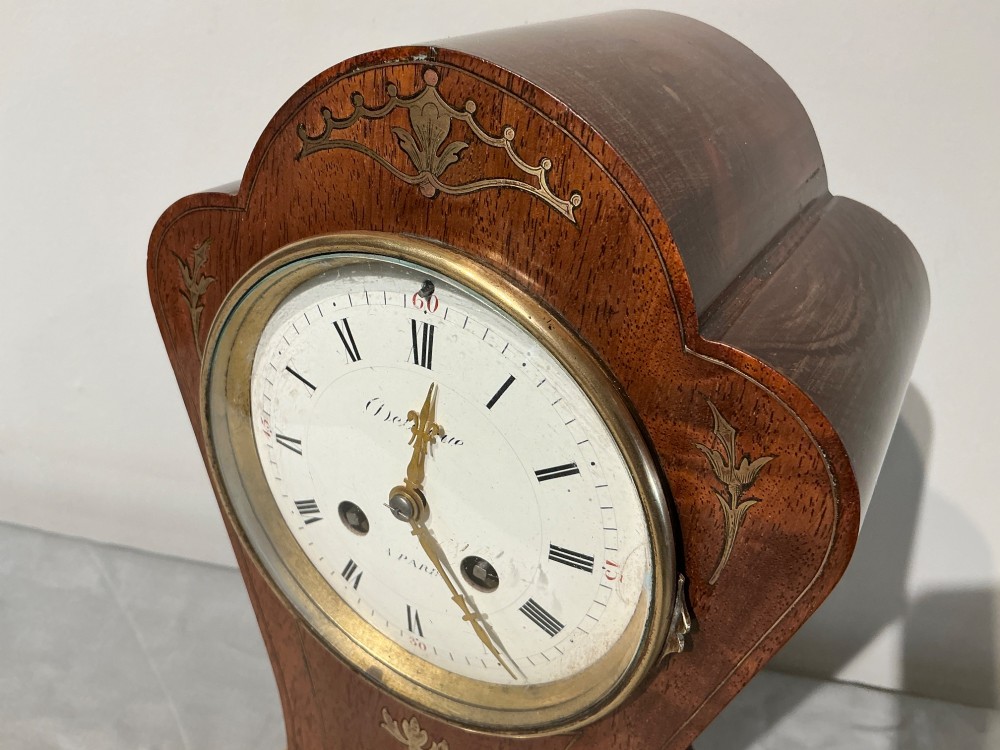 An antique balloon-shaped mahogany mantel clock featuring inlaid brass floral details, a white enamel dial with Roman numerals, and a brass-trimmed plinth base. View III