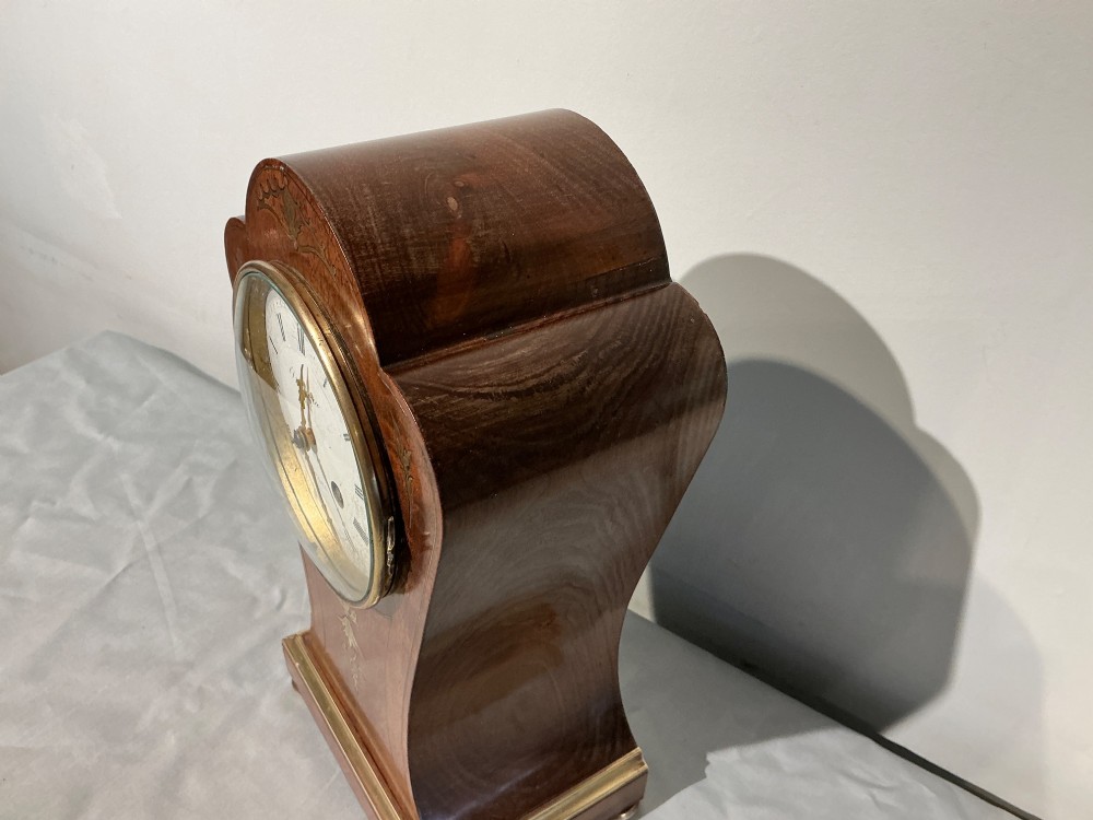 An antique balloon-shaped mahogany mantel clock featuring inlaid brass floral details, a white enamel dial with Roman numerals, and a brass-trimmed plinth base. View VI