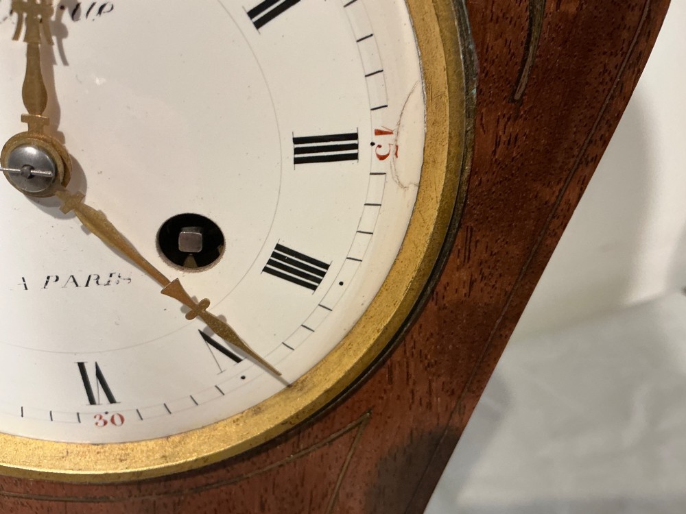 An antique balloon-shaped mahogany mantel clock featuring inlaid brass floral details, a white enamel dial with Roman numerals, and a brass-trimmed plinth base. View VIII