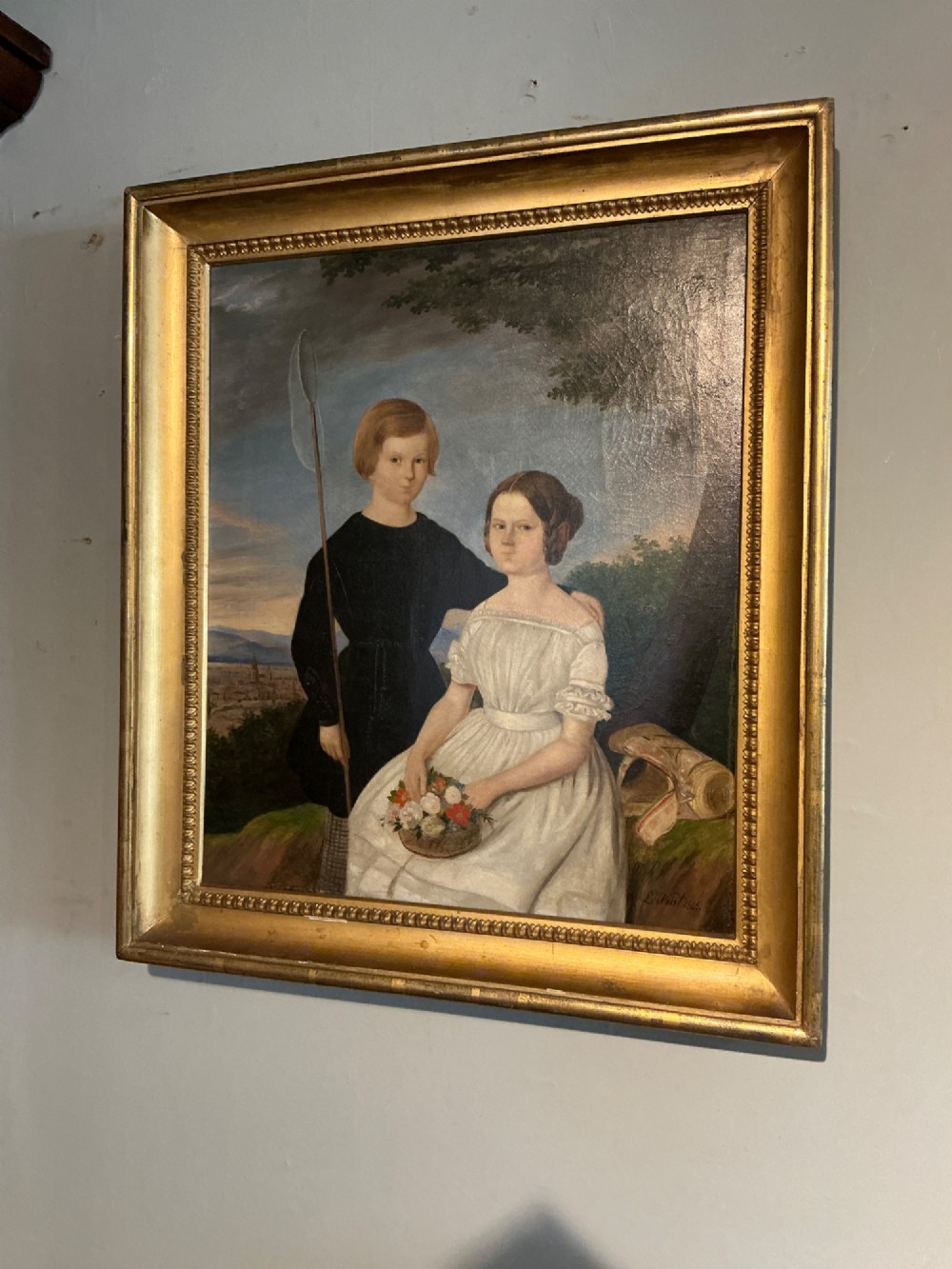 An early 19th-century oil painting depicting a boy in black clothing and a girl in a white dress seated outdoors, set within a gilded moulded frame. View II
