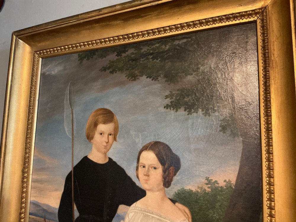 An early 19th-century oil painting depicting a boy in black clothing and a girl in a white dress seated outdoors, set within a gilded moulded frame. View VI