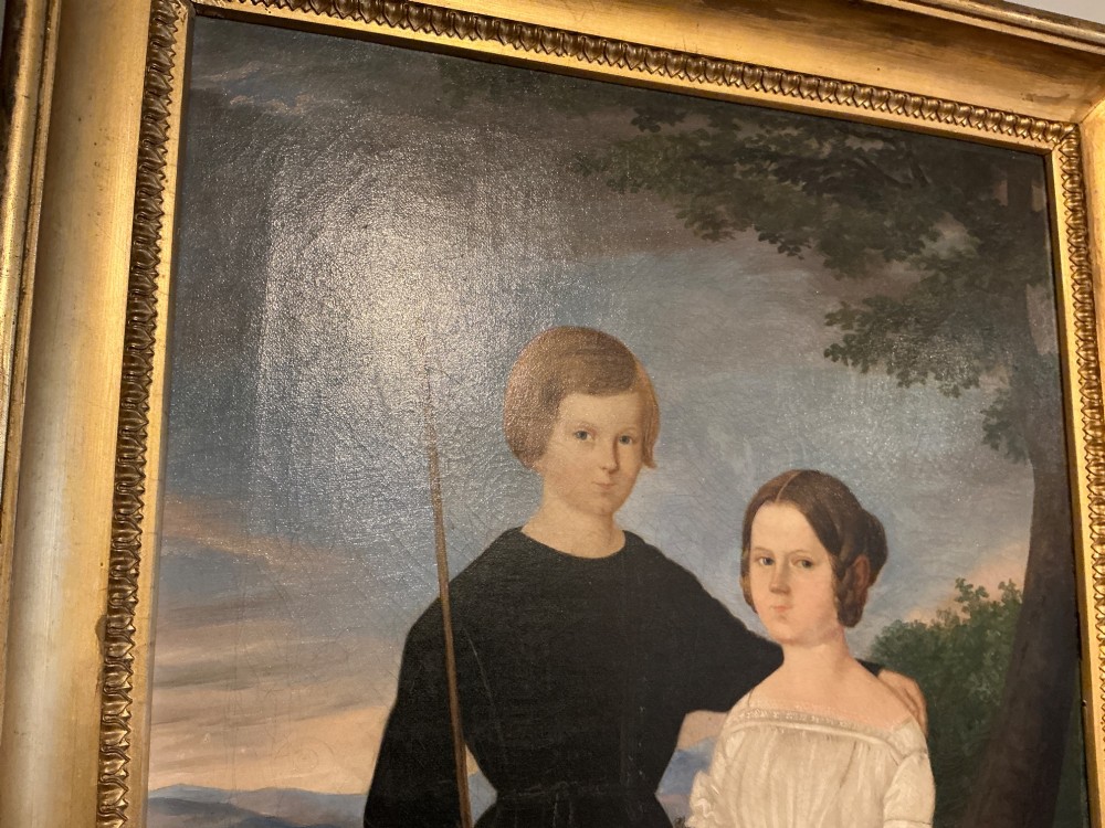 An early 19th-century oil painting depicting a boy in black clothing and a girl in a white dress seated outdoors, set within a gilded moulded frame. View IX