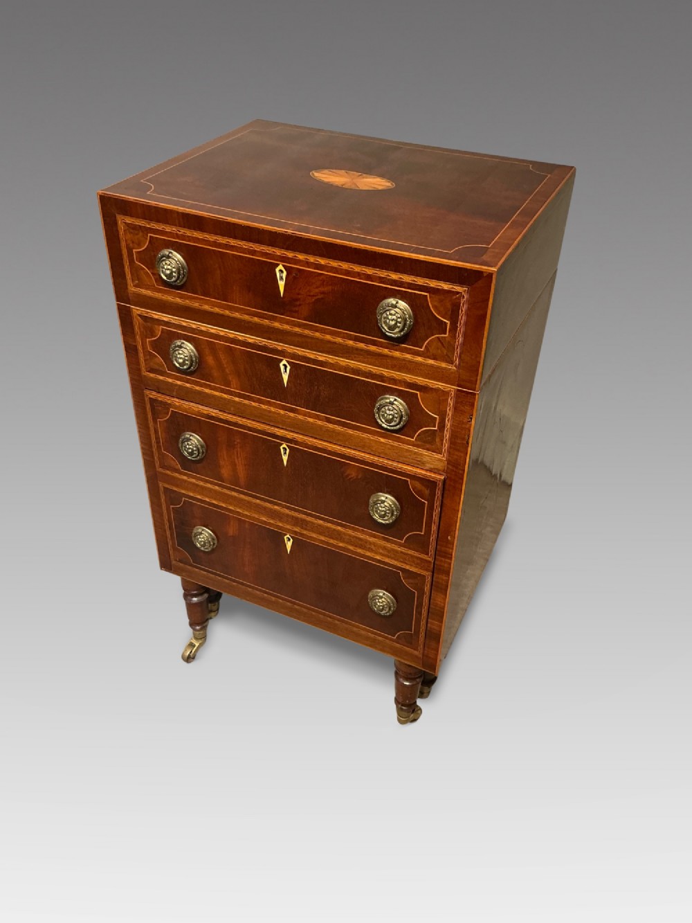 A nineteenth-century mahogany work table featuring satinwood inlay, bone escutcheons, brass ring handles, four drawer fronts, and turned legs on brass castors.