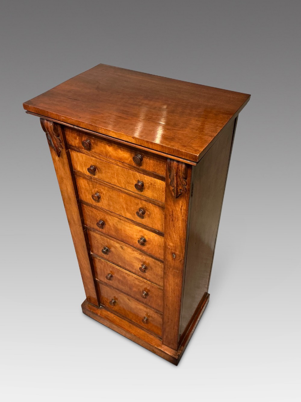 A tall, narrow Victorian walnut Wellington chest featuring seven stacked drawers with turned knobs, carved brackets, and a hinged locking pilaster. View II