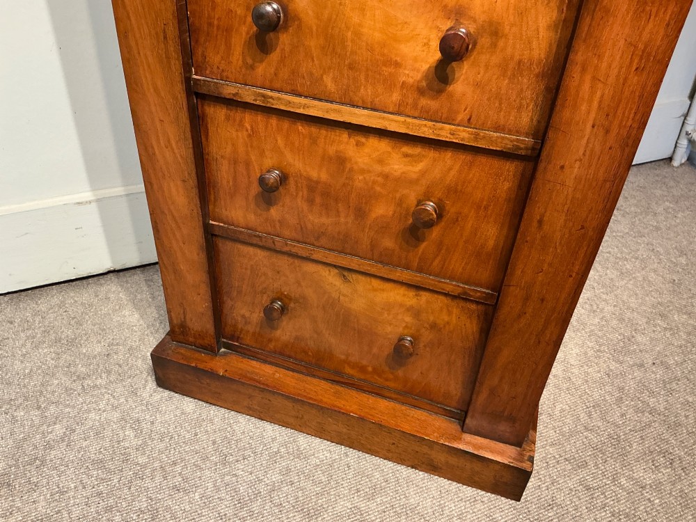 A tall, narrow Victorian walnut Wellington chest featuring seven stacked drawers with turned knobs, carved brackets, and a hinged locking pilaster. View VI