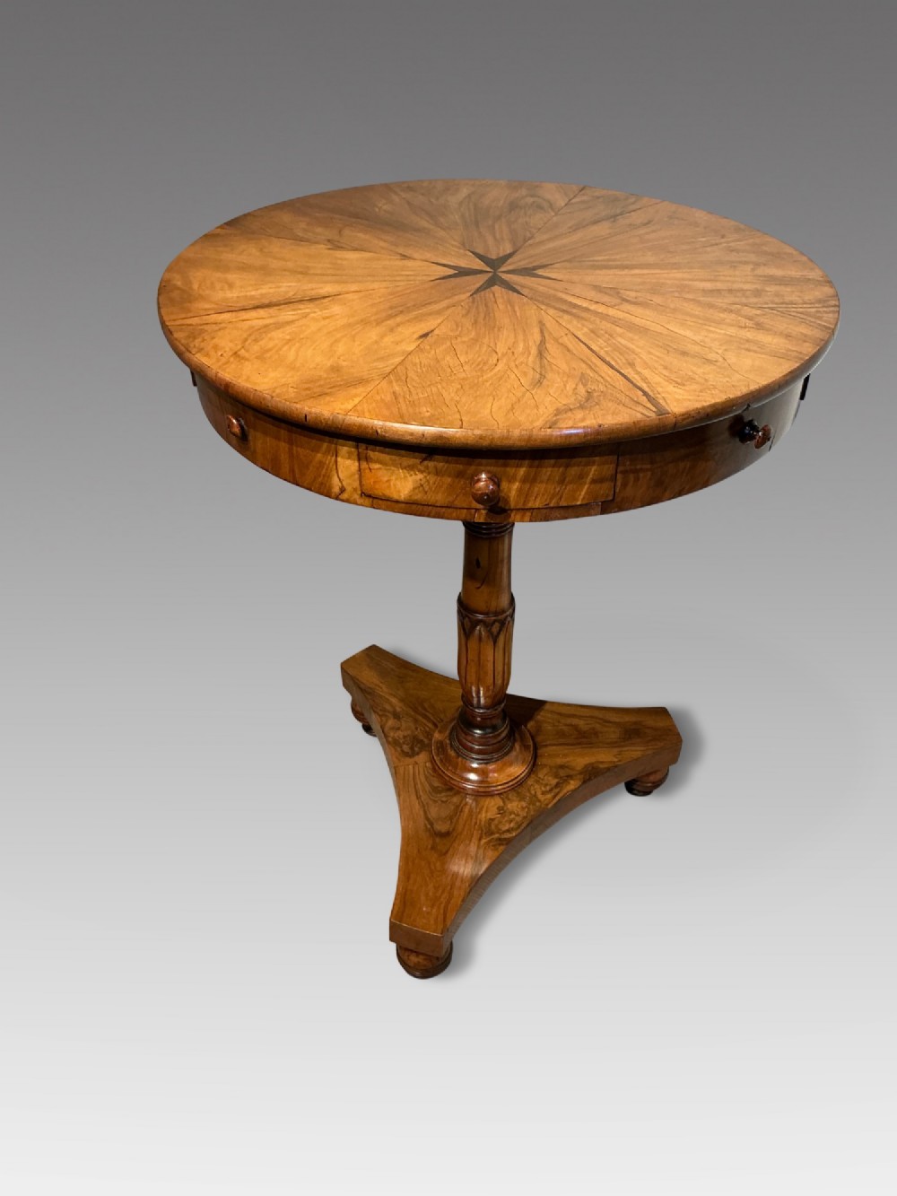 A circular antique Maltese olive wood drum table featuring a starburst veneered top with a central inlaid Maltese cross, supported on a turned central pedestal and a triform plinth base with bun feet.