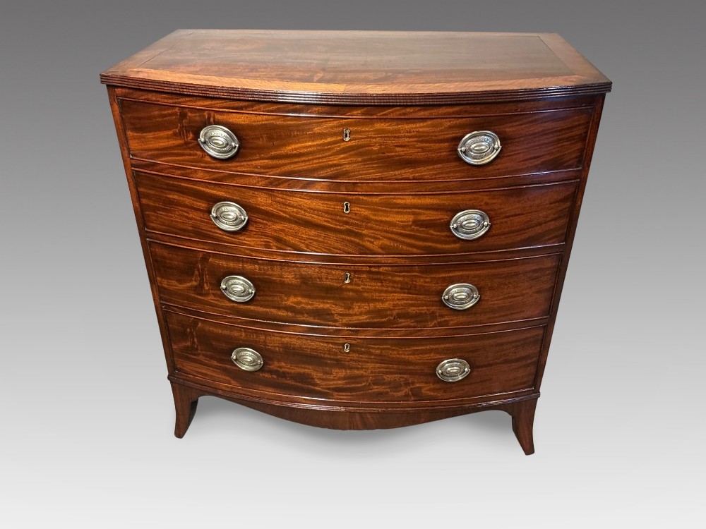 A Georgian flame mahogany bowfront chest of drawers featuring four graduated drawers with oval brass handles and splayed bracket feet.