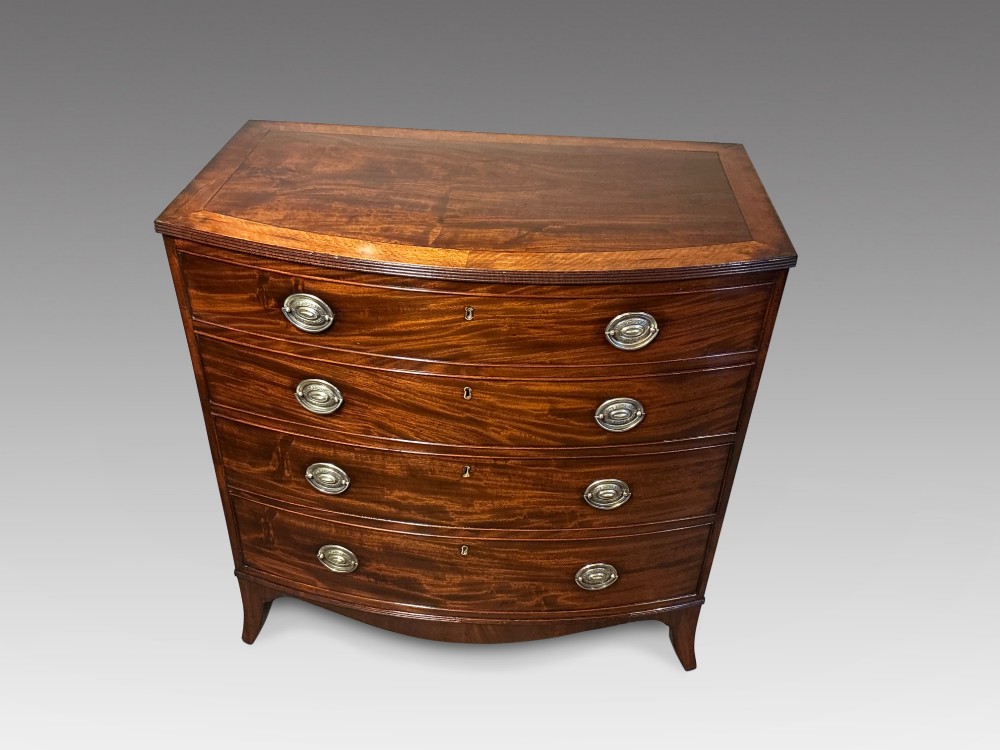 A Georgian flame mahogany bowfront chest of drawers featuring four graduated drawers with oval brass handles and splayed bracket feet. View II