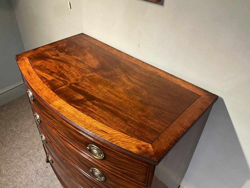 A Georgian flame mahogany bowfront chest of drawers featuring four graduated drawers with oval brass handles and splayed bracket feet. View III