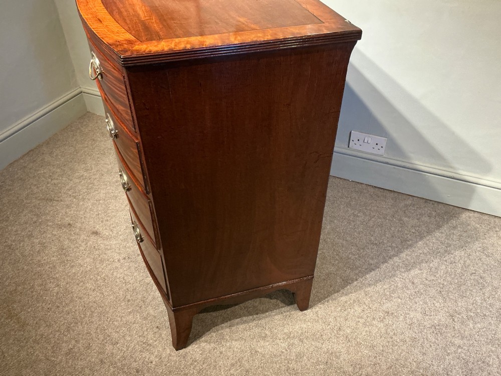 A Georgian flame mahogany bowfront chest of drawers featuring four graduated drawers with oval brass handles and splayed bracket feet. View XI