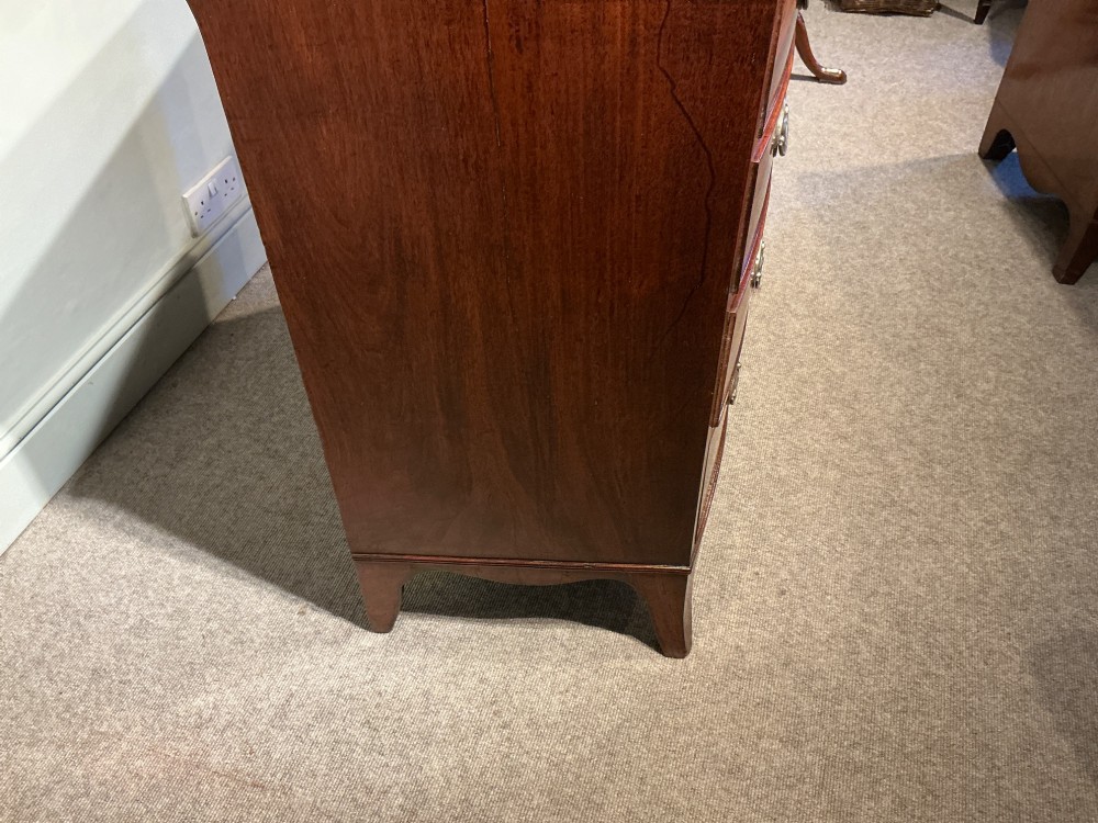 A Georgian flame mahogany bowfront chest of drawers featuring four graduated drawers with oval brass handles and splayed bracket feet. View XV