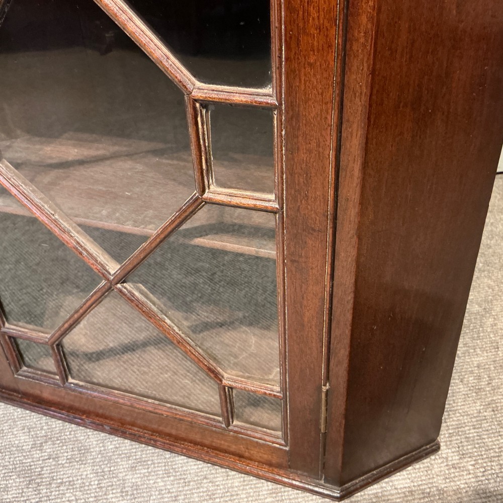An antique Georgian dark mahogany hanging corner cabinet featuring a single door with geometric astragal glazing and internal wooden shelves. View III