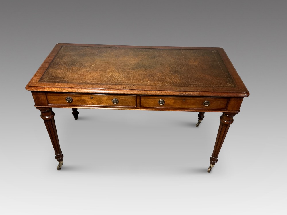 An antique mahogany writing table with a brown leather inset writing top, two frieze drawers with brass handles, and turned reeded legs on brass castors. View II