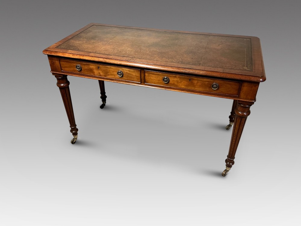 An antique mahogany writing table with a brown leather inset writing top, two frieze drawers with brass handles, and turned reeded legs on brass castors. View III