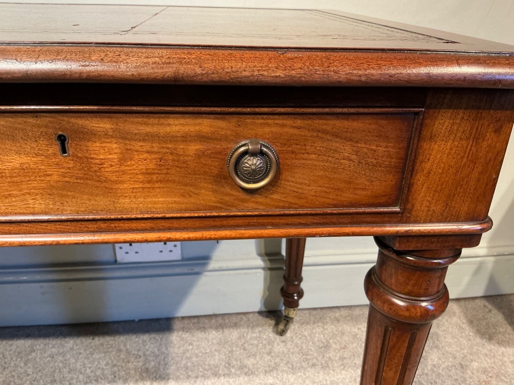 An antique mahogany writing table with a brown leather inset writing top, two frieze drawers with brass handles, and turned reeded legs on brass castors. View VII