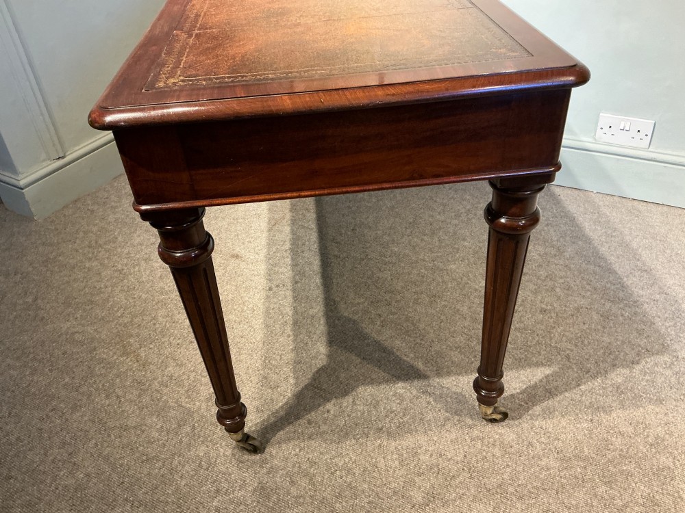 An antique mahogany writing table with a brown leather inset writing top, two frieze drawers with brass handles, and turned reeded legs on brass castors. View X