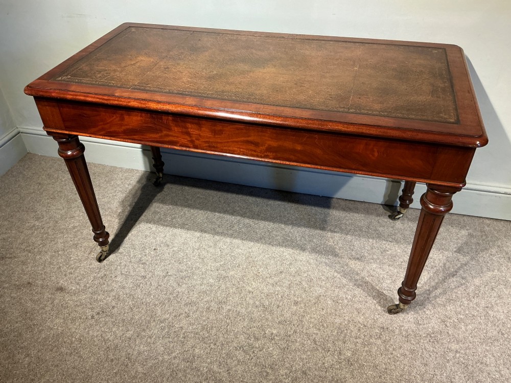 An antique mahogany writing table with a brown leather inset writing top, two frieze drawers with brass handles, and turned reeded legs on brass castors. View XI