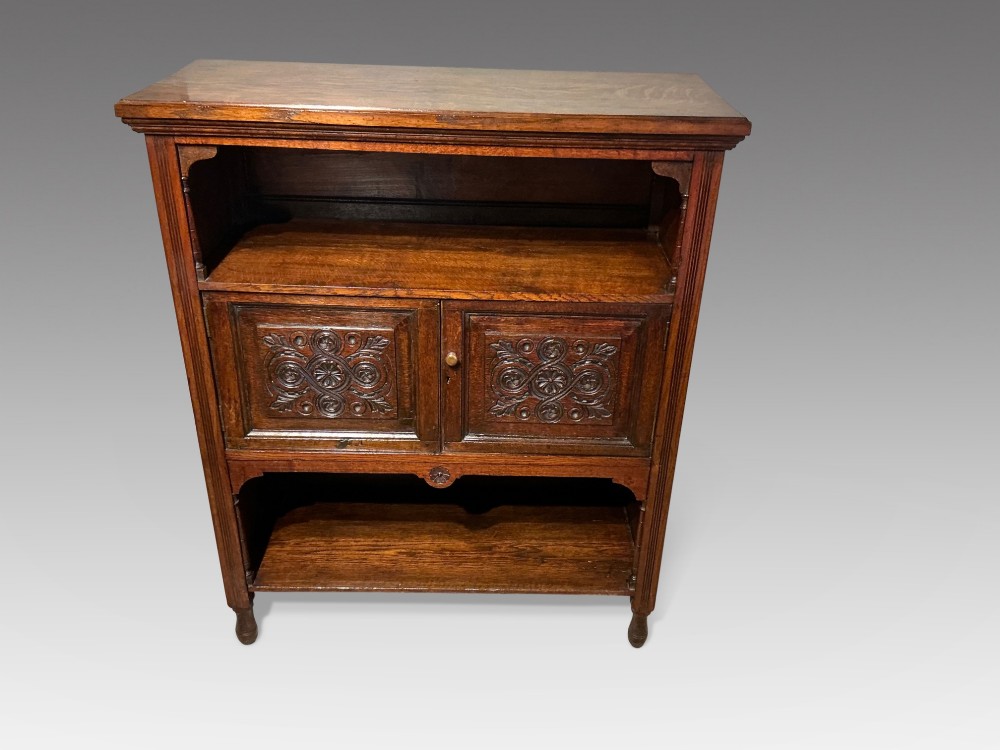 A Victorian dark oak low bookcase featuring two hand-carved panel doors in the centre positioned between upper and lower open storage shelves.