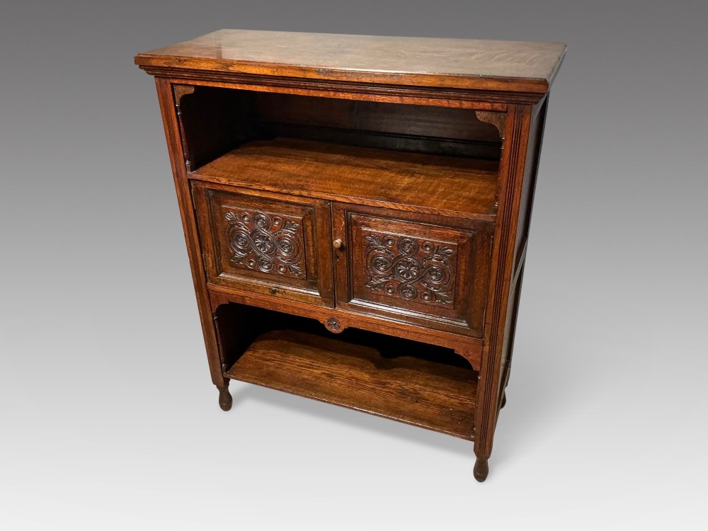 A Victorian dark oak low bookcase featuring two hand-carved panel doors in the centre positioned between upper and lower open storage shelves. View II