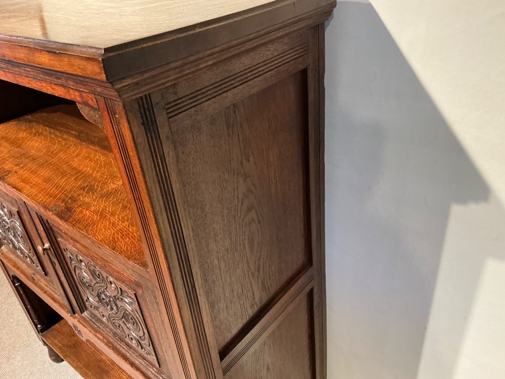 A Victorian dark oak low bookcase featuring two hand-carved panel doors in the centre positioned between upper and lower open storage shelves. View VI