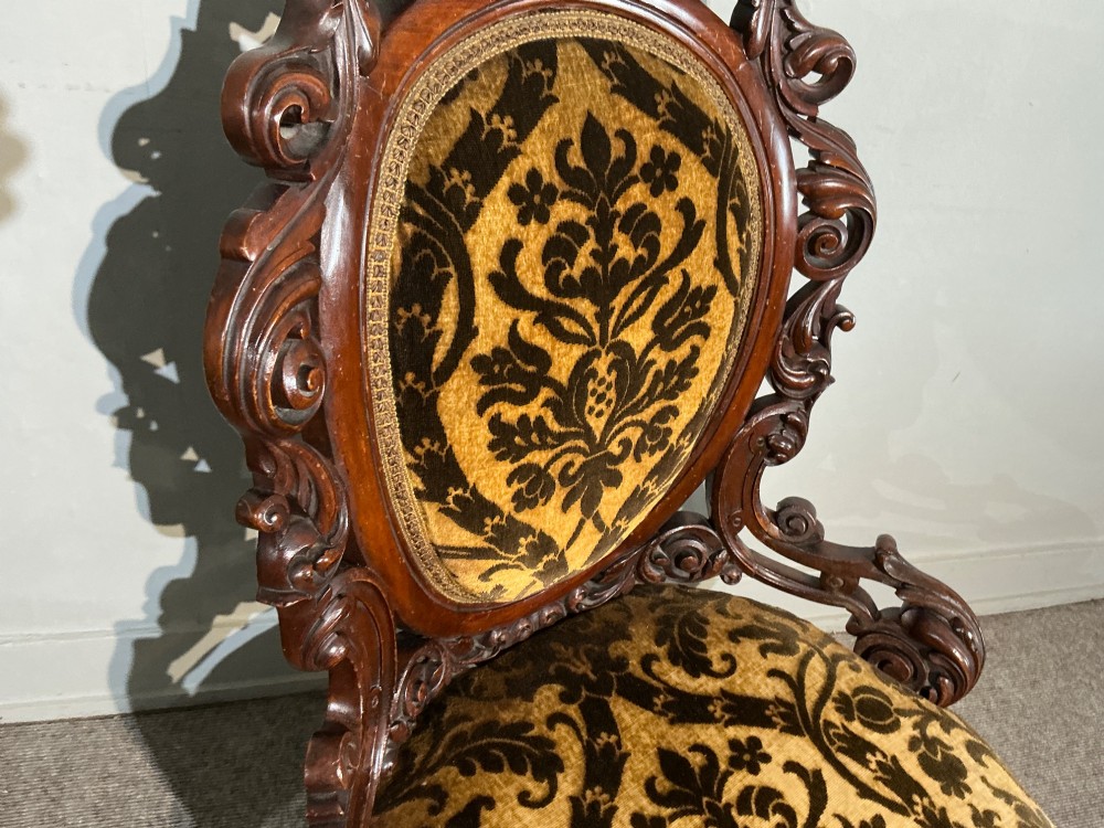 A Victorian mahogany salon chair featuring an ornate carved scrollwork frame, oval backrest, circular seat upholstered in gold and black velvet damask fabric, and turned legs with castors. View IV
