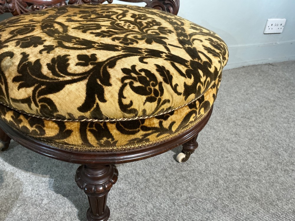 A Victorian mahogany salon chair featuring an ornate carved scrollwork frame, oval backrest, circular seat upholstered in gold and black velvet damask fabric, and turned legs with castors. View VII