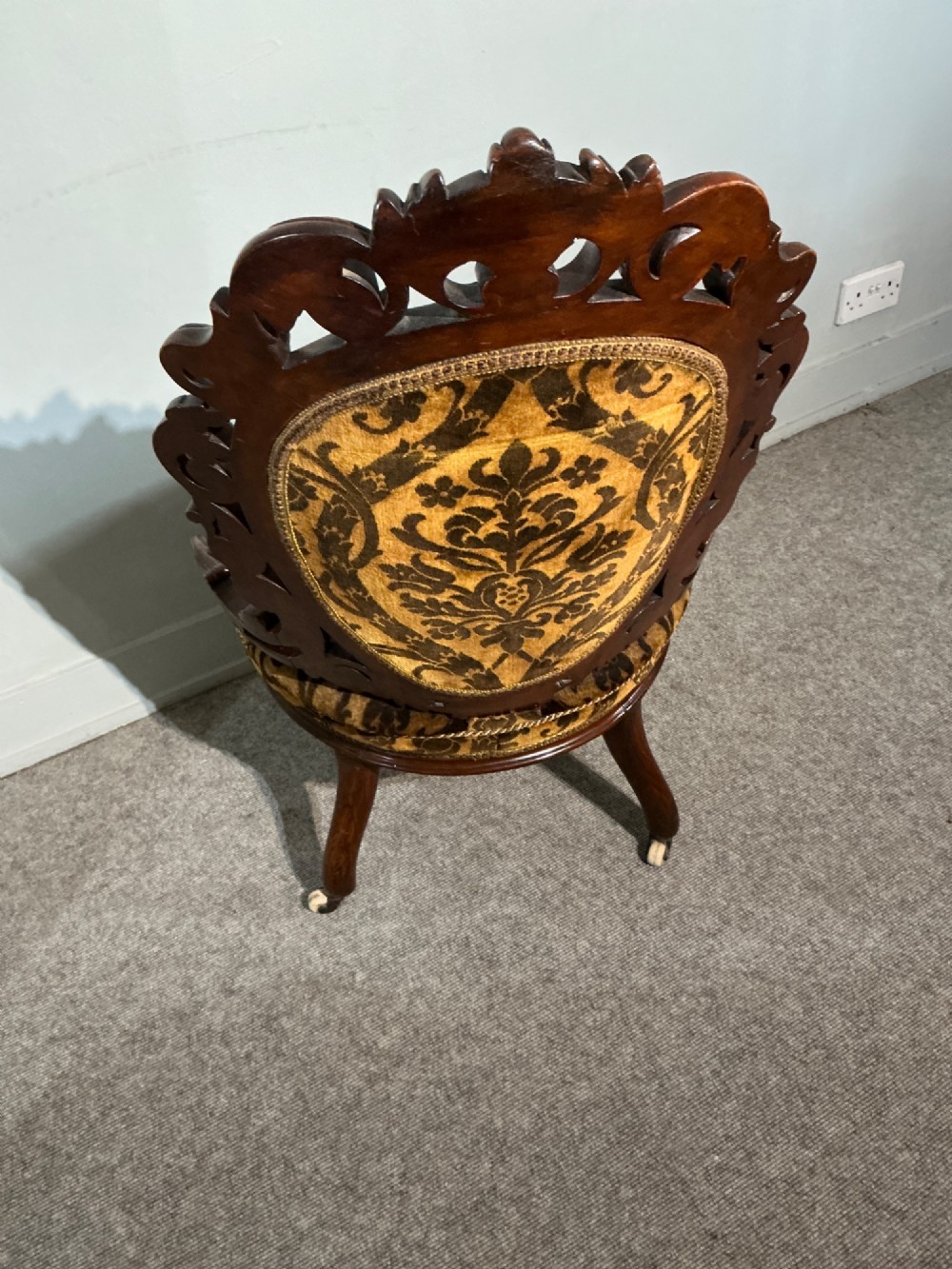 A Victorian mahogany salon chair featuring an ornate carved scrollwork frame, oval backrest, circular seat upholstered in gold and black velvet damask fabric, and turned legs with castors. View VIII