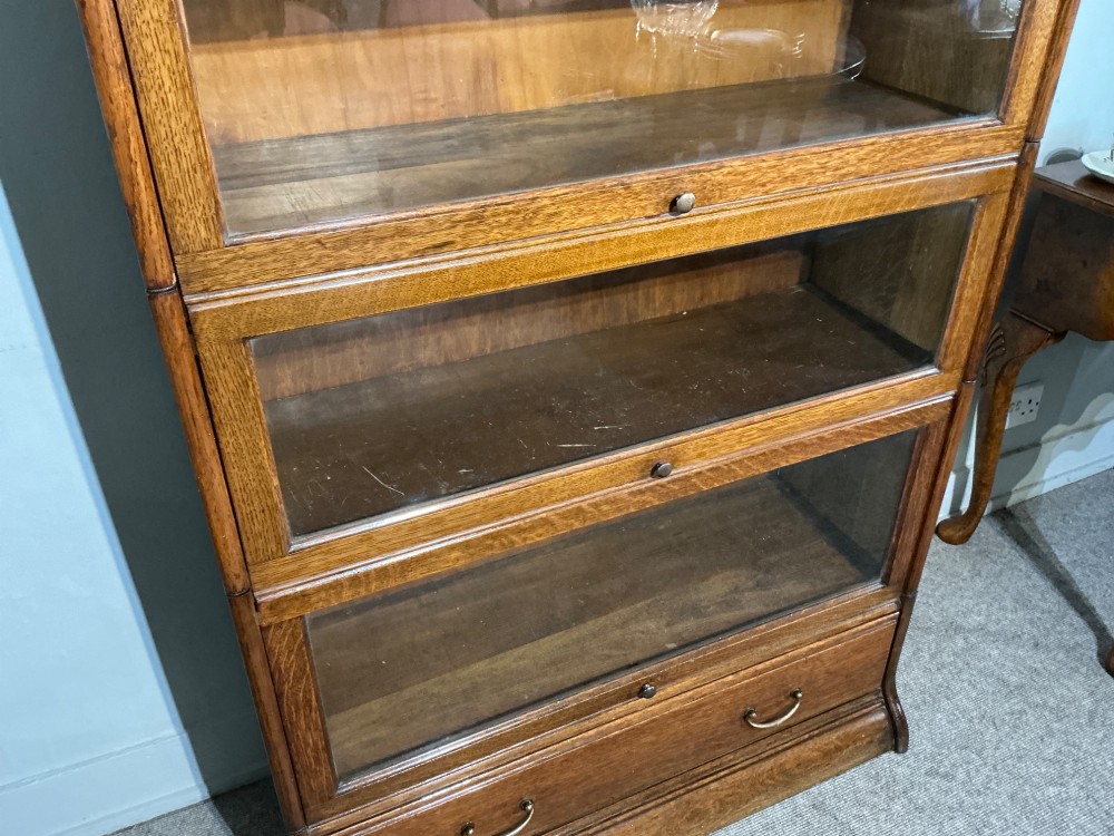 A 1920s oak three-tier sectional bookcase featuring glazed lift-up doors and a single drawer at the base. View V