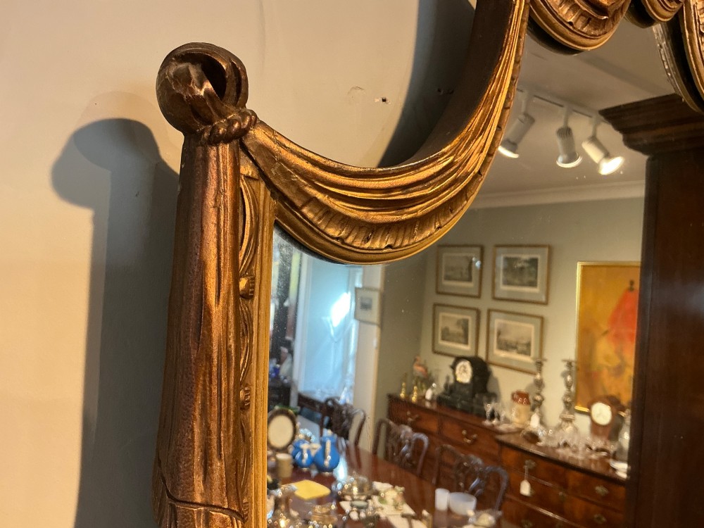 An Edwardian shield-shaped wall mirror featuring a giltwood frame decorated with carved draped swags and a central rosette crest. View III