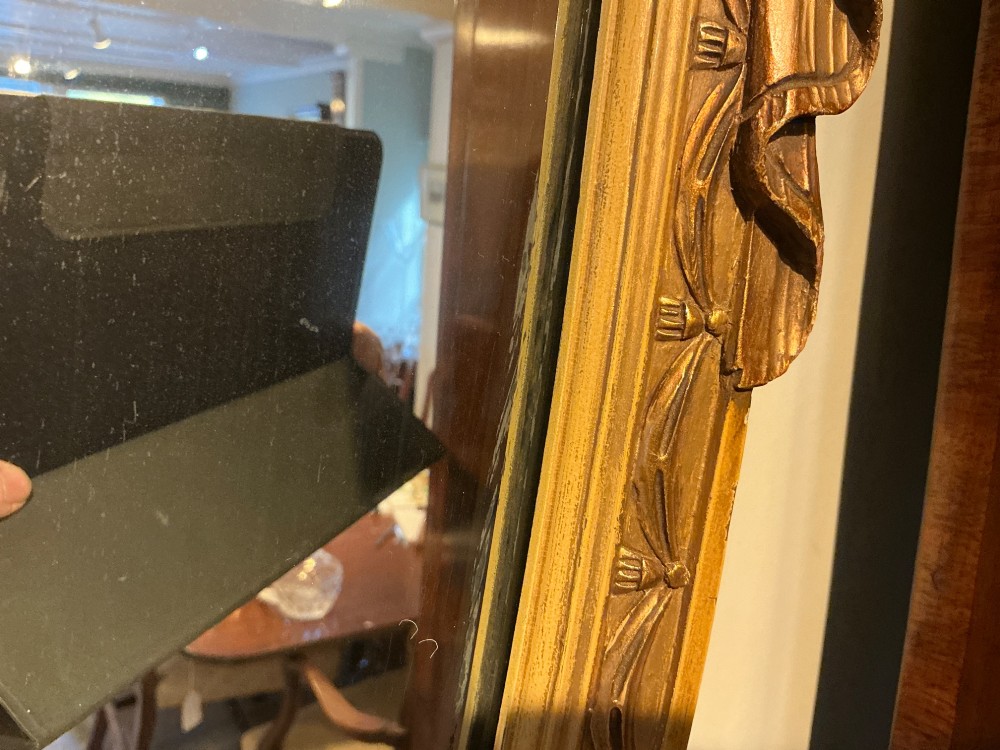 An Edwardian shield-shaped wall mirror featuring a giltwood frame decorated with carved draped swags and a central rosette crest. View VII