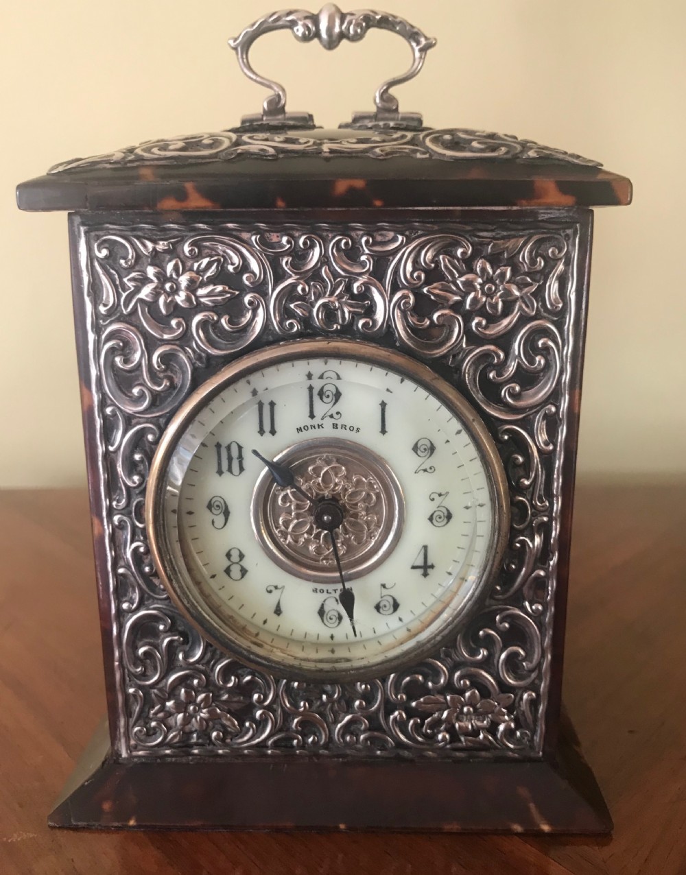 A 19th-century Victorian mantel clock featuring a dark tortoiseshell case, a silver front panel with floral scrollwork, a top carrying handle, and a white circular dial. View II