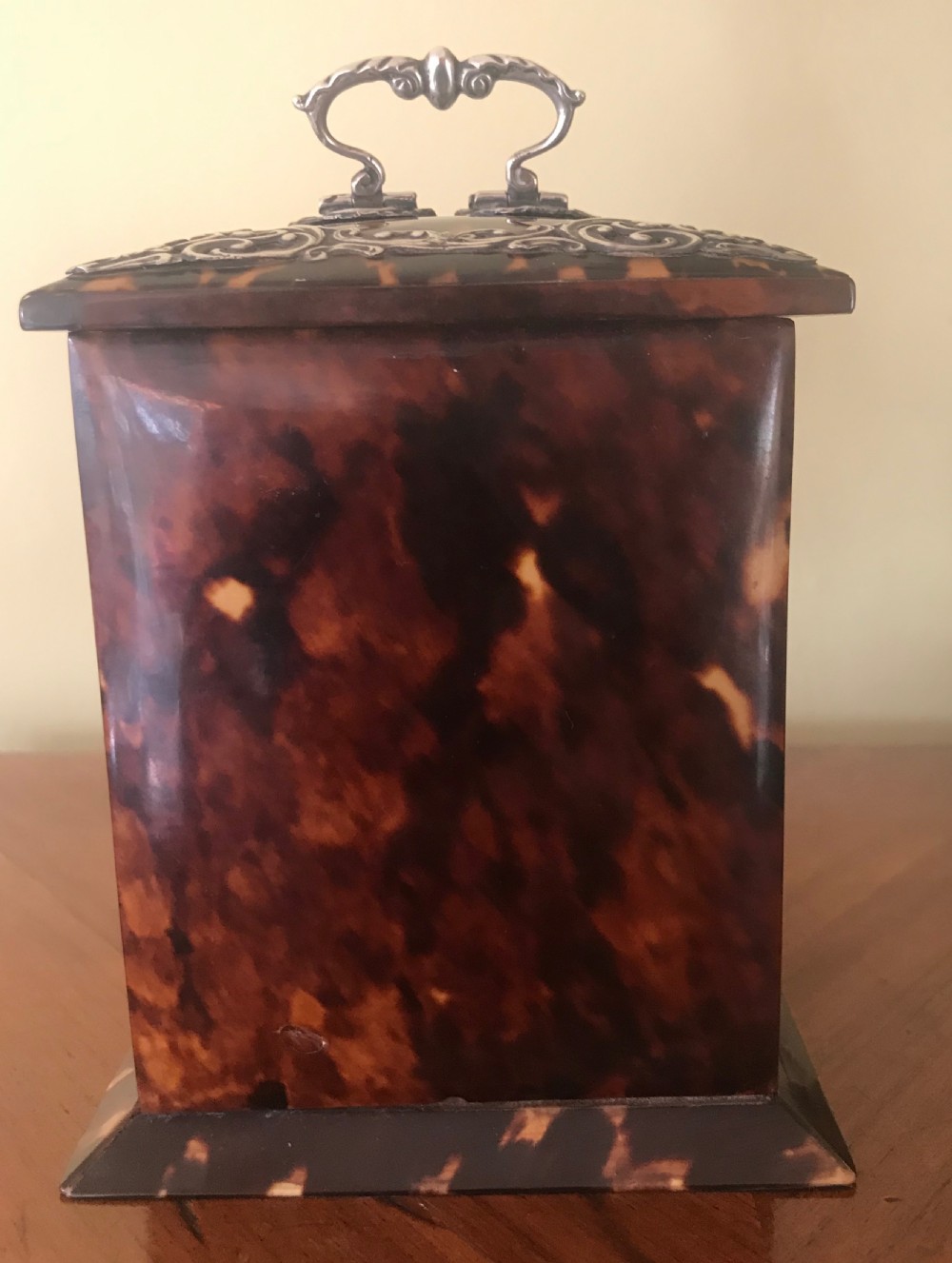 A 19th-century Victorian mantel clock featuring a dark tortoiseshell case, a silver front panel with floral scrollwork, a top carrying handle, and a white circular dial. View IV
