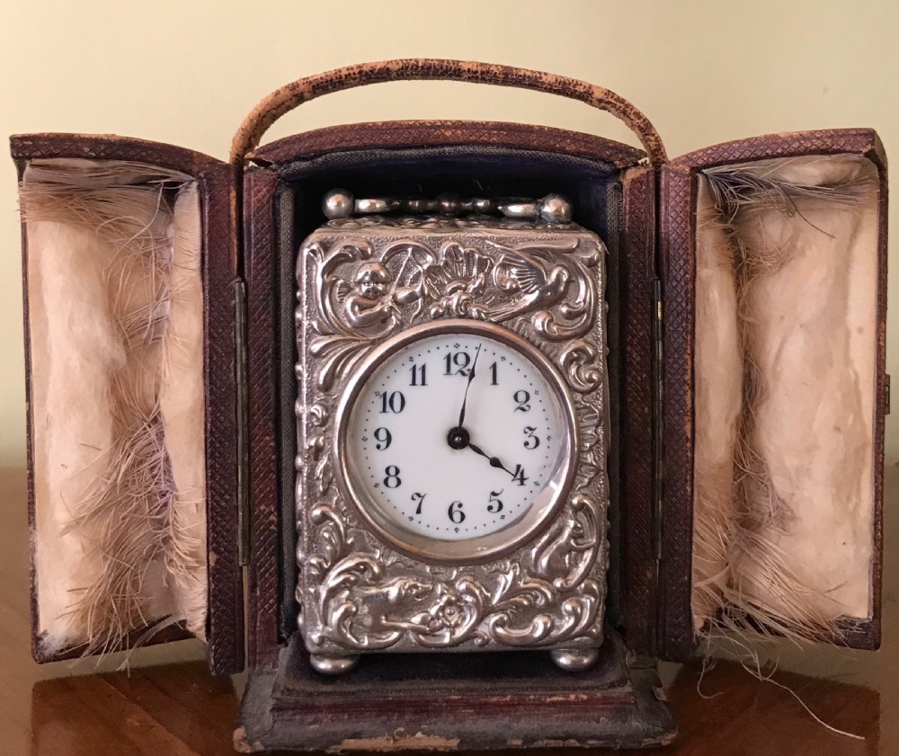 A 19th-century miniature silver clock with detailed relief ornamentation, displayed inside an open brown leather travel case.