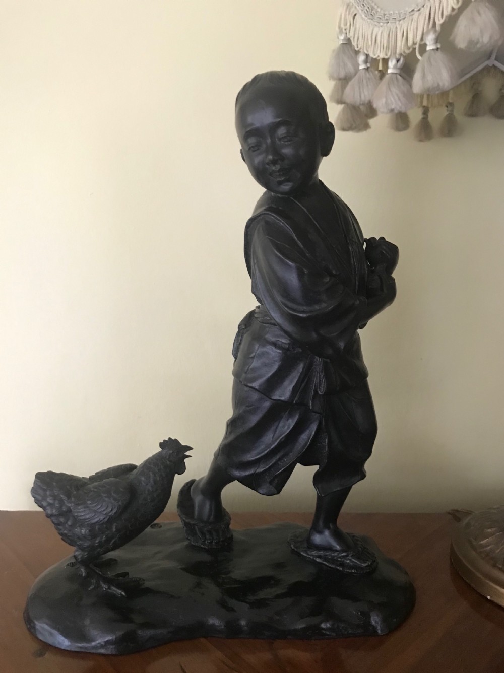 A dark bronze Japanese okimono sculpture depicting a boy in traditional kimono and geta sandals walking beside a chicken on a cast naturalistic base.