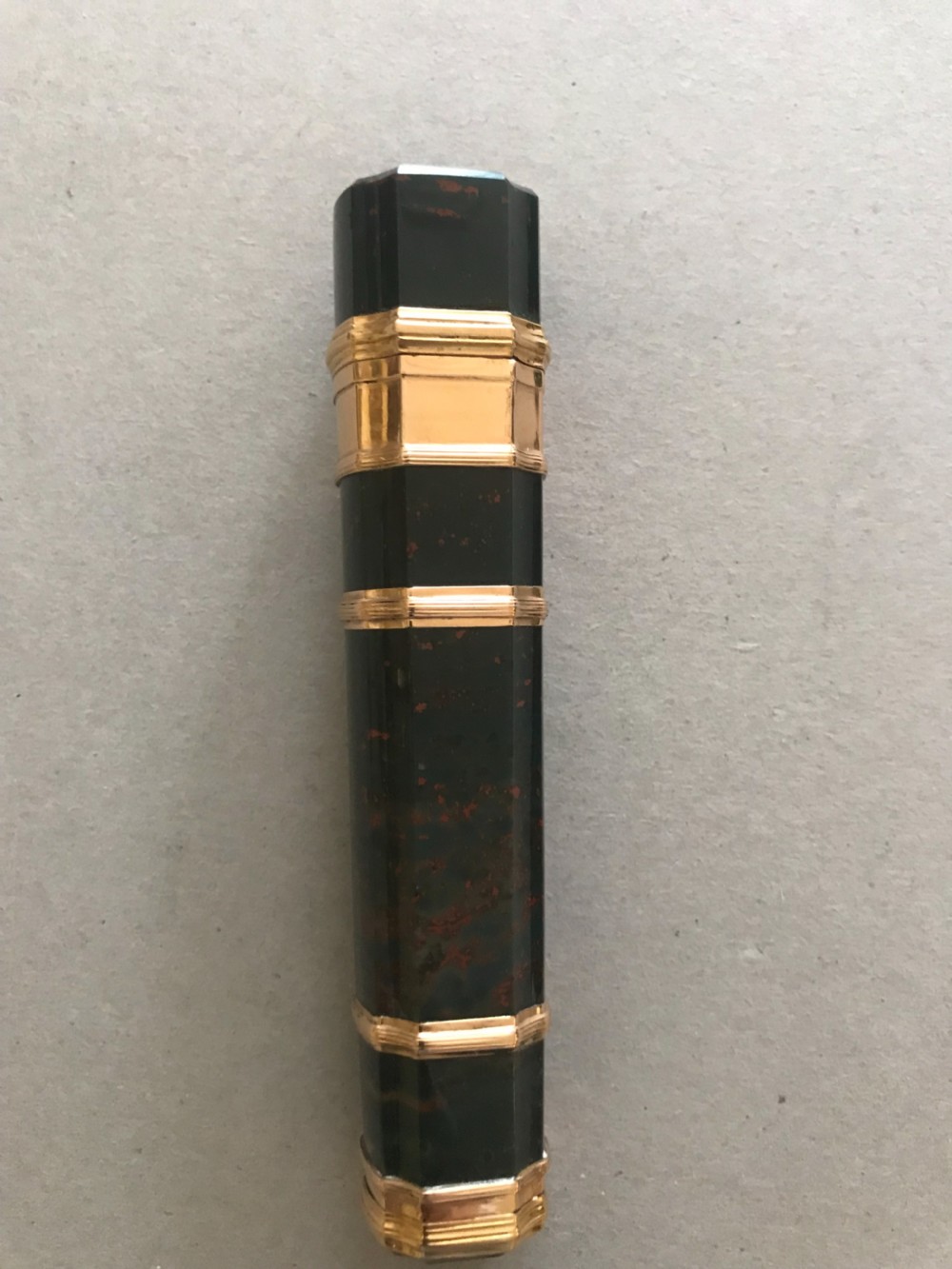 A cylindrical dark green bloodstone etui featuring reeded gold mounts, subtle red mineral inclusions, and a stone-set push-button catch. View II
