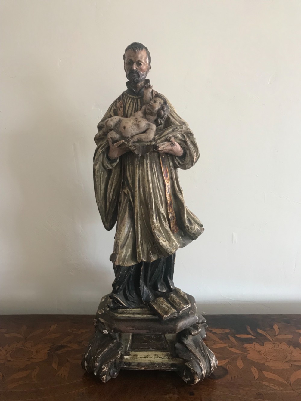 A late 18th-century polychromed wood carving depicting a standing bearded saint holding an infant, set upon a carved pedestal base.